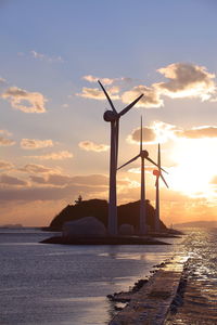 Windmill by sea against sky during sunset