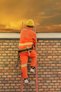 Man working against orange sky