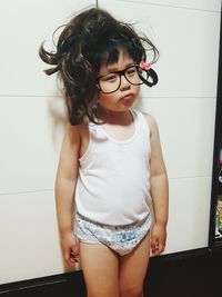 Portrait of boy wearing wig standing against wall at home