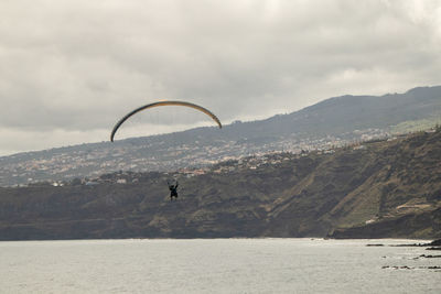 Person paragliding over sea against sky