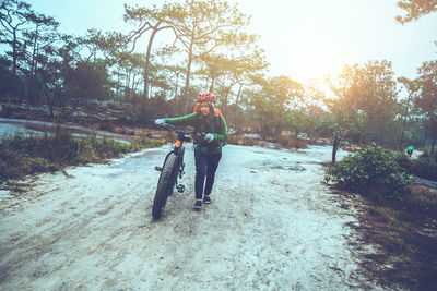 Woman pushing bicycle on dirt road against trees