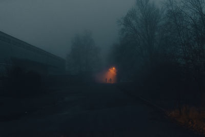 Road by silhouette trees against sky in city