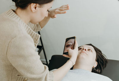 A girl cosmetologist takes pictures of a client s eyelashes on a smartphone.