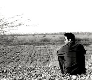 Rear view of woman sitting on field against clear sky