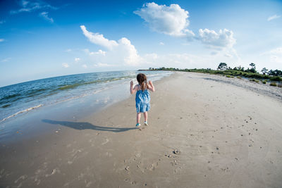 Rear view of girl jumping on beach against sky