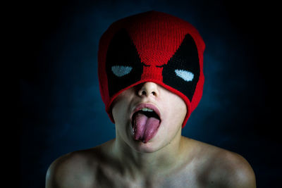 Young man making face while wearing red mask against black background