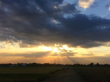 Road amidst field against sky during sunset