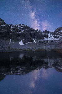 Scenic view of lake by snowcapped mountains against sky at night