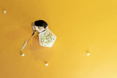 High angle view of girl holding badminton racket an cock against yellow background