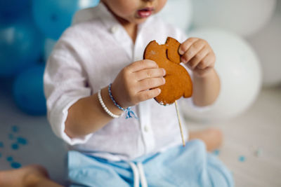 Baby boy in blue pants and shirt standing on the floor next to the cake in blue and white balloons