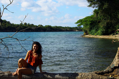 Young woman sitting by sea against sky