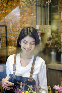 Smiling florist working in store seen through glass window