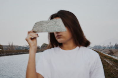 Woman holding mirror against lake