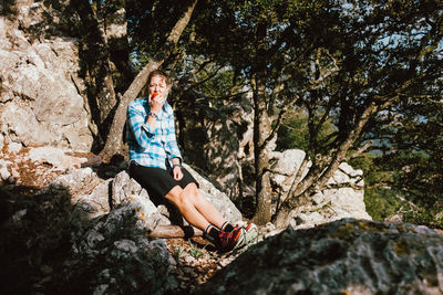 Portrait of woman eating apple while sitting on rock against trees