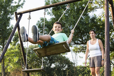 Boy enjoying swing by mother at park