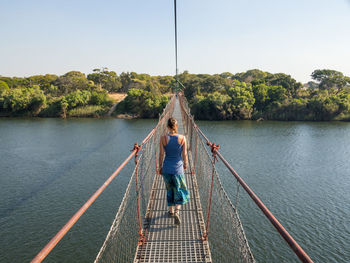 Rear view of person standing on rope against river