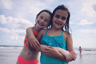 Cute friends standing on shore against sea at beach