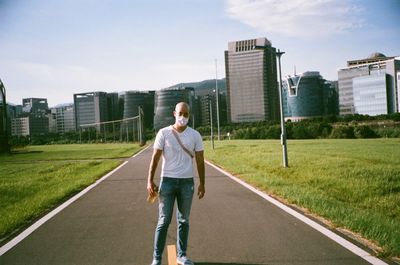 Full length of man standing on grass in city against sky