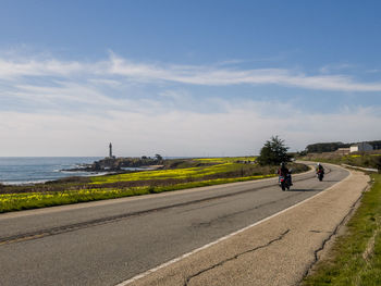 Rear view of people riding bicycle on road against sky