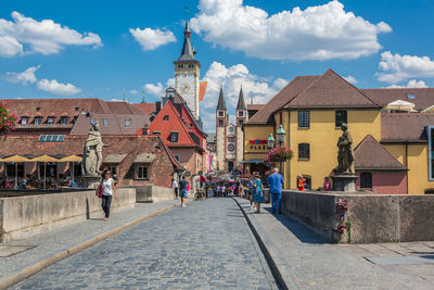 People on street amidst buildings in city against sky