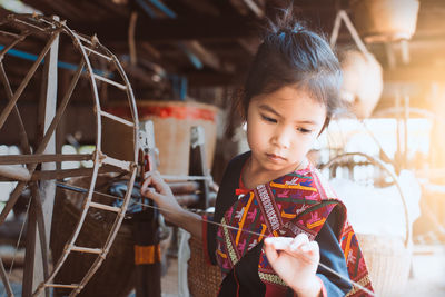 Cute girl in traditional clothing using wooden spinning wheel at workshop