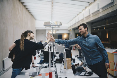 Male and female computer programmers giving high-five over desk in office