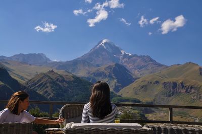 Women sitting in restaurant against mountains and sky during sunny day