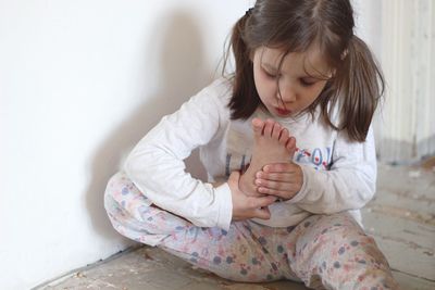 Cute girl holding foot while sitting at home