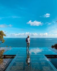 Man standing on glass against sea and sky