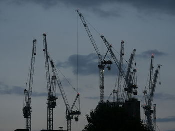 Low angle view of cranes at construction site against cloudy sky