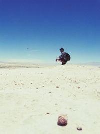 Full length of man crouching in desert against clear blue sky