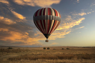 Hot air balloon flying over field against sky during sunset