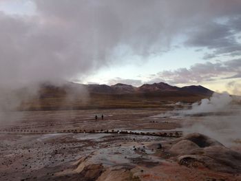 Smoke emitting from volcanic mountain against cloudy sky