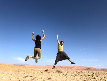 Low angle view of men jumping against clear sky