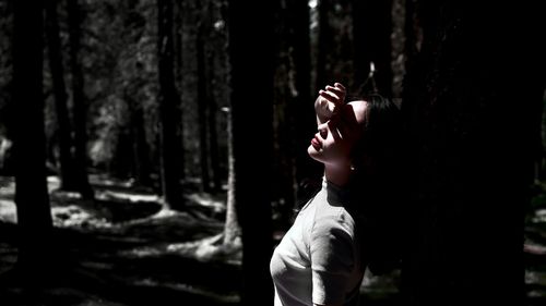 Young woman standing against tree trunk