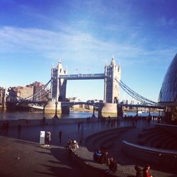 People on bridge in city against sky