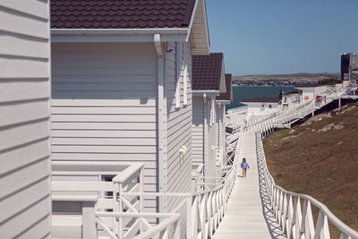 Boy child in a striped blue sailor jacket walks on the street among white wooden houses by the sea