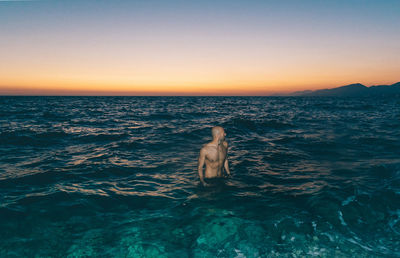 Shirtless man standing in sea against clear sky at night