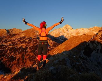 Woman with arms outstretched standing on mountain against sky