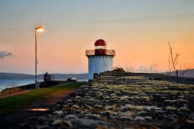 Lighthouse by sea against clear sky during sunset