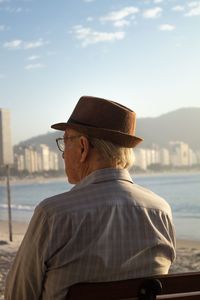 Side view of man wearing hat sitting looking at sea