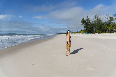 Rear view of woman walking at beach against sky