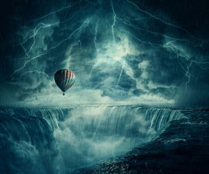 Hot air balloon fly over the chasm of a foggy waterfall below a dark stormy sky.