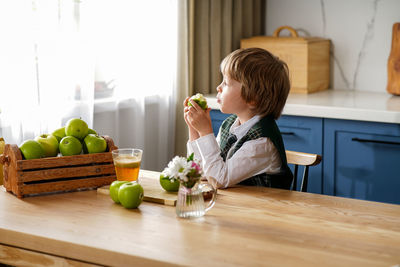 Thoughtful schoolboy is having breakfast with fresh juice and apple waiting for the school bus