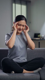 Side view of young woman sitting on sofa at home