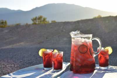 Cold iced tea made from hibiscus flower petal tea in drink glasses and pitcher in hot desert setting