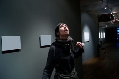 Young woman looking away while standing against wall at home