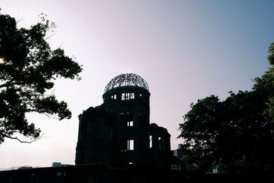 Low angle view of silhouette trees and building against sky