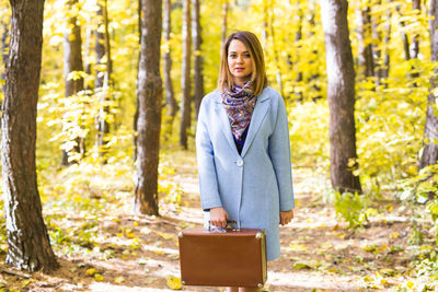 Young woman standing by tree trunk in forest during autumn