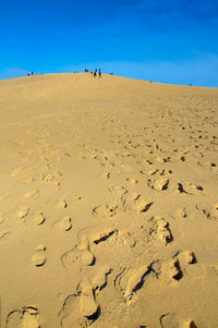 Footprints on sand at beach against blue sky